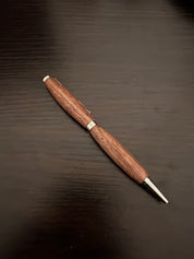Wooden pen with silver accents on a dark wooden surface